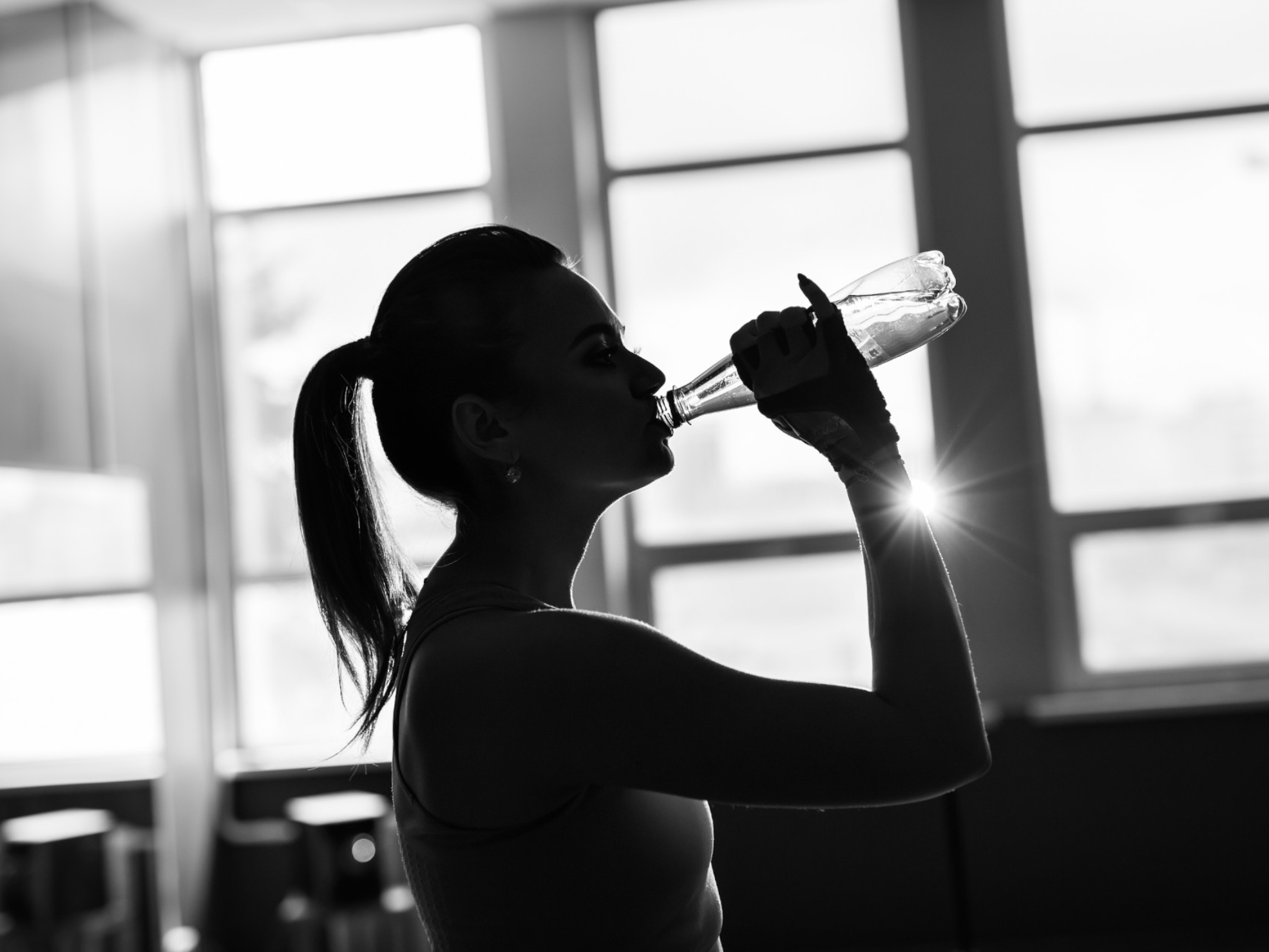 Młoda kobieta pijąca wodę podczas treningu na siłowni - nawodnienie